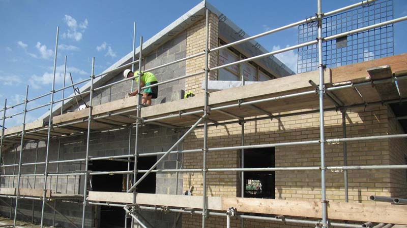 man on scaffolding laying bricks to build a house